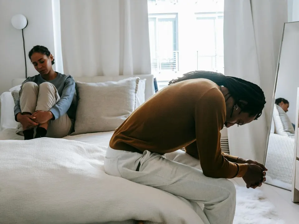 Zwei Menschen sitzen niedergeschlagen und voneinander abgewandt auf einem Bett
